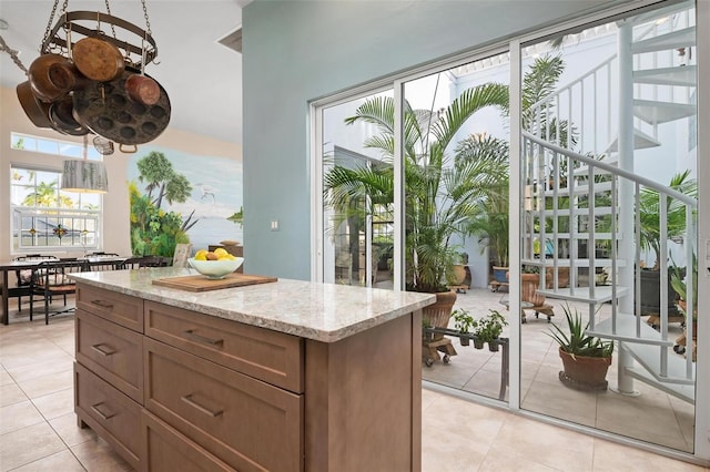 kitchen with light stone counters, decorative light fixtures, a kitchen island, and light tile patterned flooring