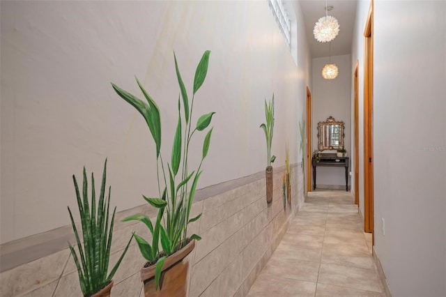 hall featuring light tile patterned flooring, a notable chandelier, and tile walls