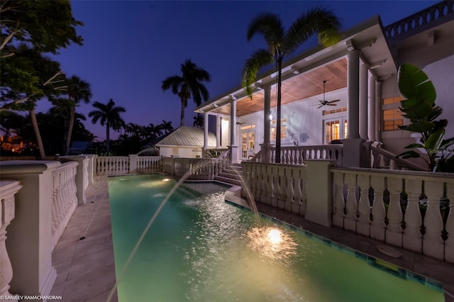 pool at night with ceiling fan, pool water feature, and a patio