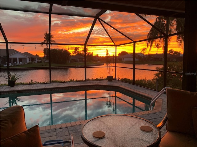 pool at dusk featuring a water view, a patio area, and a lanai