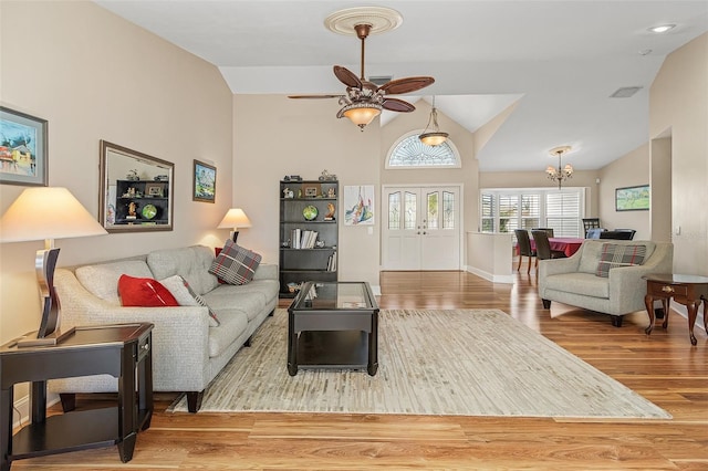 living room with lofted ceiling, ceiling fan with notable chandelier, and light hardwood / wood-style flooring