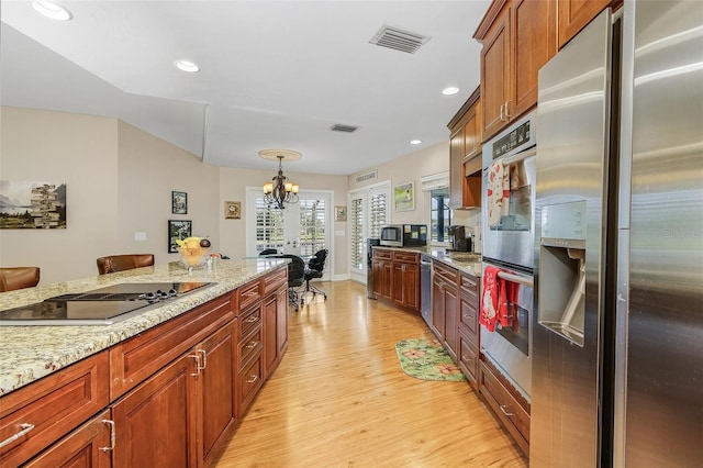 kitchen featuring appliances with stainless steel finishes, a chandelier, light stone countertops, and light wood-type flooring