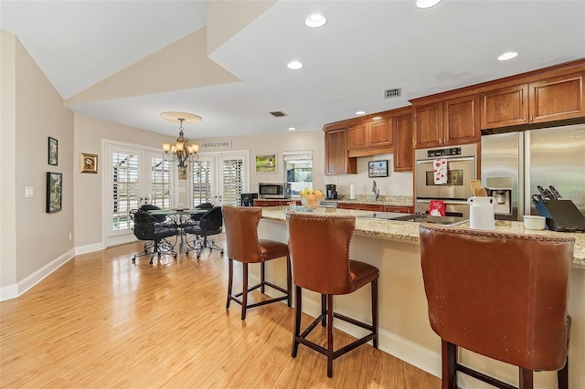 kitchen with light wood-type flooring, a breakfast bar, appliances with stainless steel finishes, and an inviting chandelier