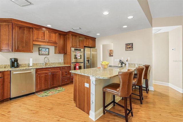 kitchen with light hardwood / wood-style floors, stainless steel appliances, a breakfast bar, light stone counters, and sink