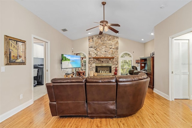 living room featuring a stone fireplace, vaulted ceiling, ceiling fan, and light wood-type flooring