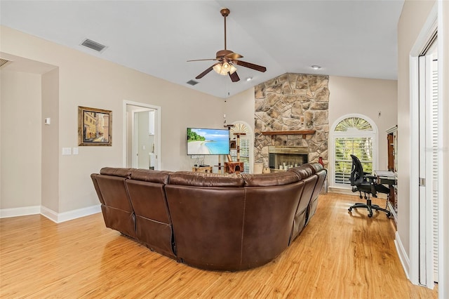 living room featuring light hardwood / wood-style floors, ceiling fan, vaulted ceiling, and a stone fireplace