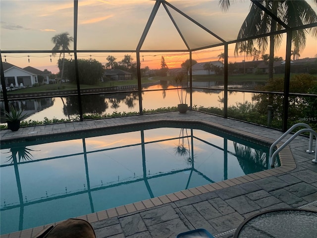 pool at dusk with glass enclosure, a patio, and a water view