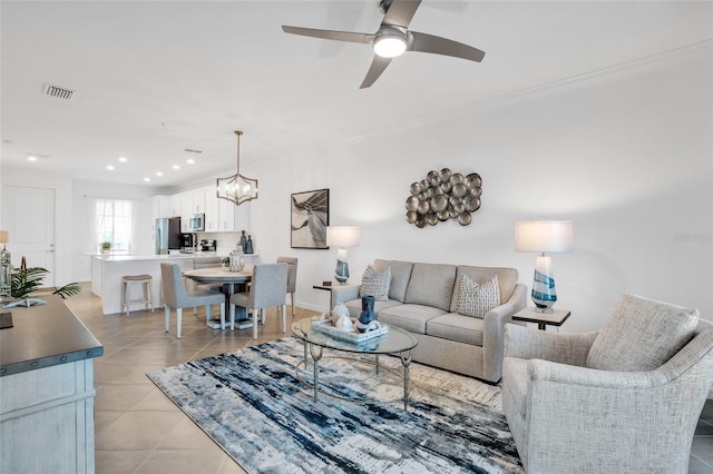 tiled living room with ceiling fan with notable chandelier and ornamental molding