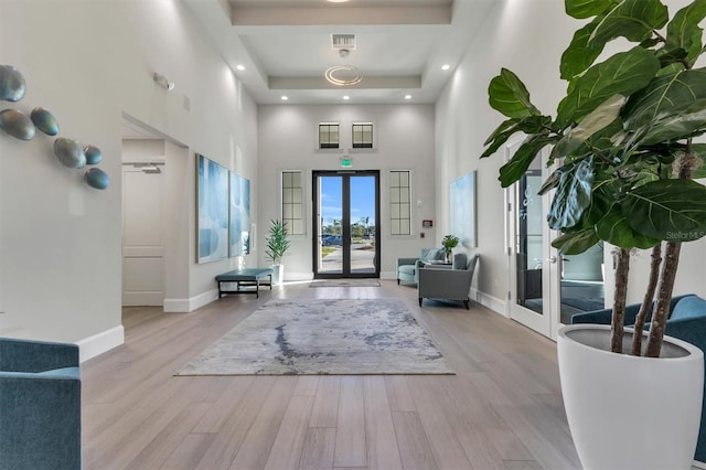 foyer featuring a raised ceiling, light hardwood / wood-style floors, french doors, and a towering ceiling