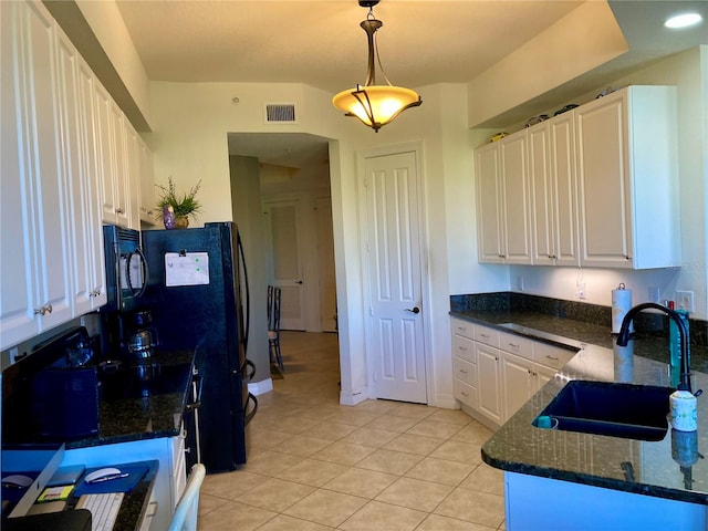 kitchen with dark stone counters, white cabinets, sink, decorative light fixtures, and light tile patterned floors