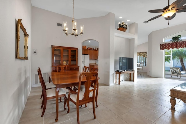 tiled dining space featuring ceiling fan with notable chandelier and a towering ceiling