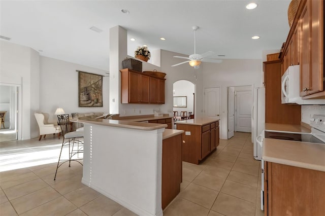 kitchen featuring ceiling fan, light tile flooring, white appliances, a center island, and a breakfast bar area