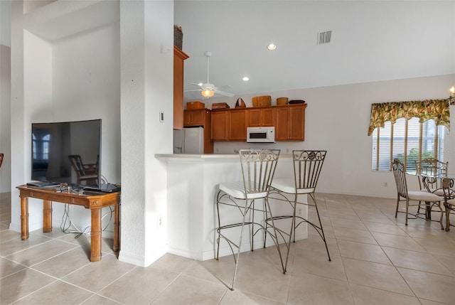 kitchen with white appliances, ceiling fan, light tile floors, hanging light fixtures, and a breakfast bar area