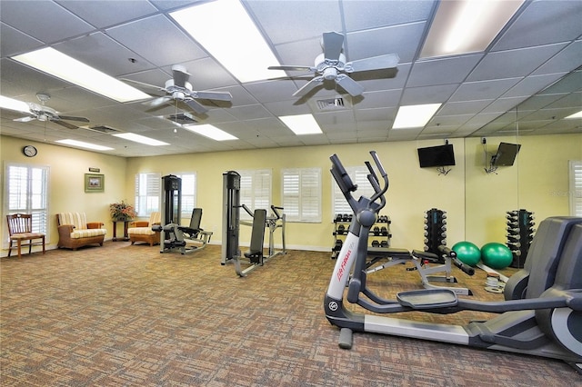 gym featuring a paneled ceiling, ceiling fan, and dark colored carpet