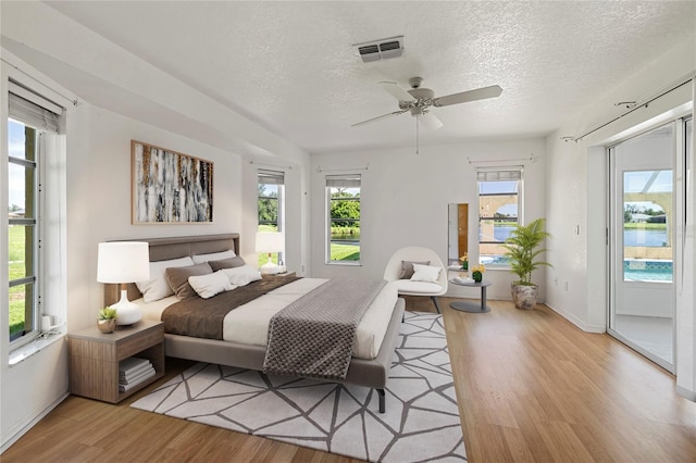 bedroom featuring ceiling fan, access to outside, light hardwood / wood-style flooring, and a textured ceiling