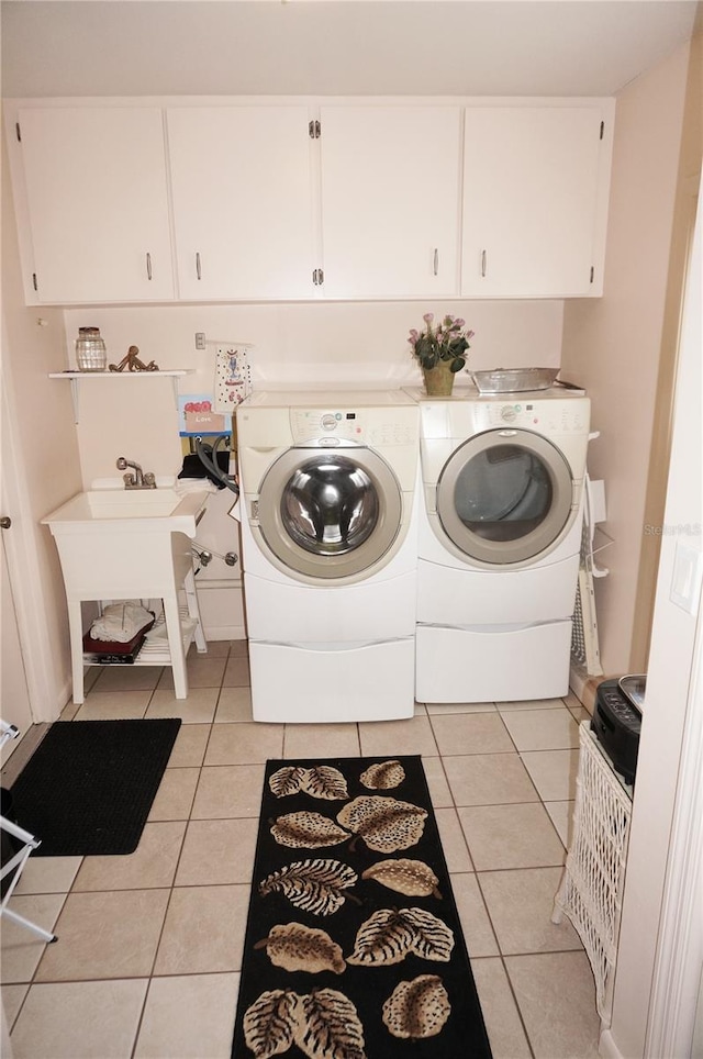 clothes washing area with independent washer and dryer, light tile floors, and cabinets