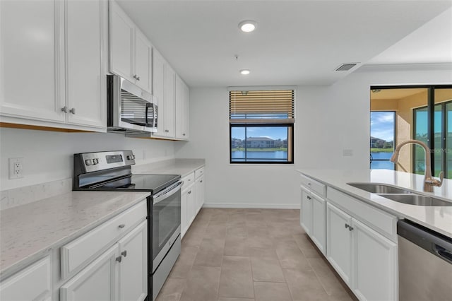 kitchen featuring light tile patterned flooring, appliances with stainless steel finishes, white cabinetry, sink, and light stone countertops