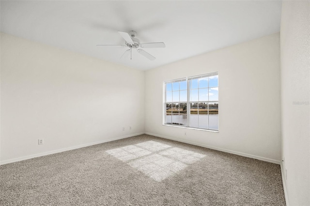 spare room with a water view, light colored carpet, and ceiling fan