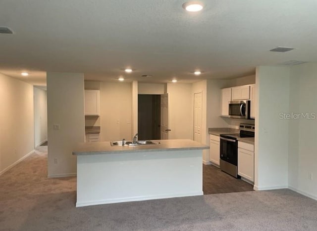 kitchen featuring dark carpet, stainless steel appliances, sink, white cabinets, and an island with sink