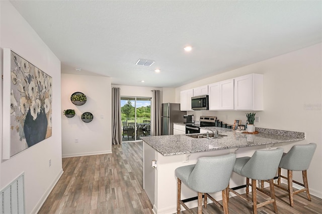 kitchen with appliances with stainless steel finishes, a breakfast bar, white cabinetry, light stone counters, and kitchen peninsula