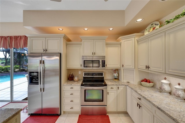 kitchen with tasteful backsplash, cream cabinets, light tile patterned flooring, and stainless steel appliances