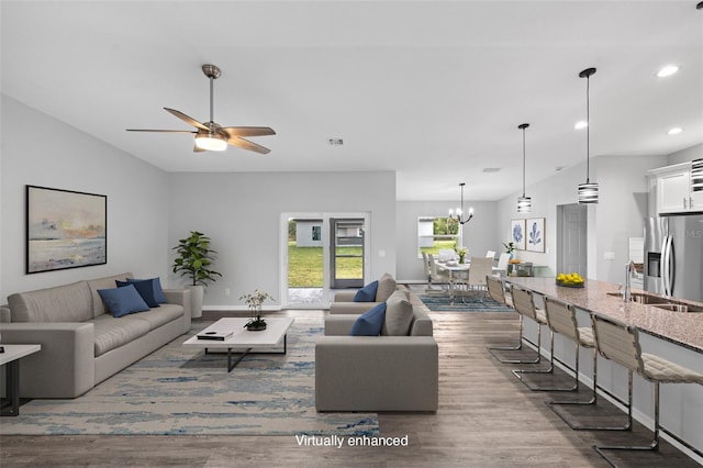 living room with sink, ceiling fan with notable chandelier, hardwood / wood-style flooring, and vaulted ceiling