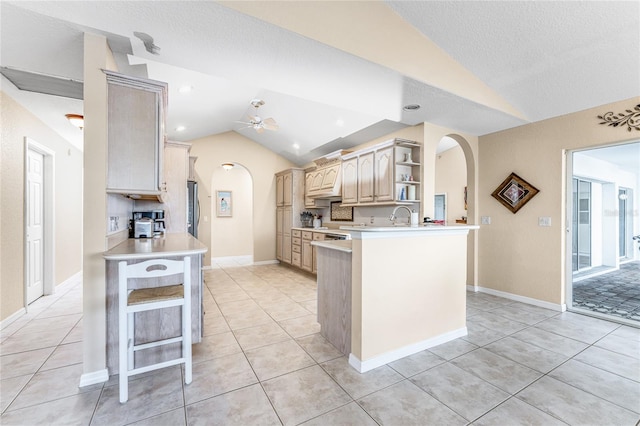 kitchen featuring ceiling fan, light brown cabinets, kitchen peninsula, vaulted ceiling, and a breakfast bar area