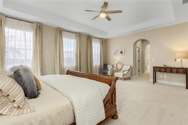 carpeted bedroom with a raised ceiling and ceiling fan