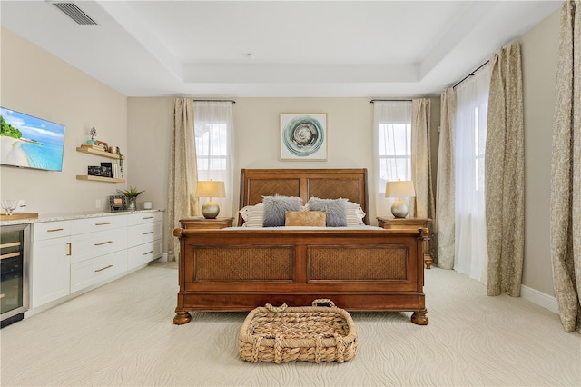 carpeted bedroom with a raised ceiling, beverage cooler, and multiple windows