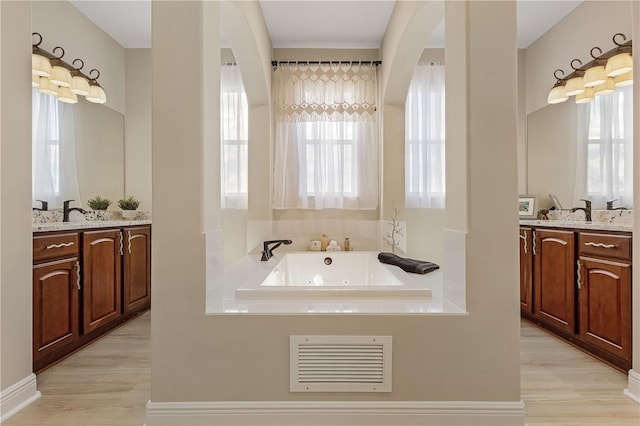 bathroom featuring a tub, oversized vanity, hardwood / wood-style flooring, and dual sinks