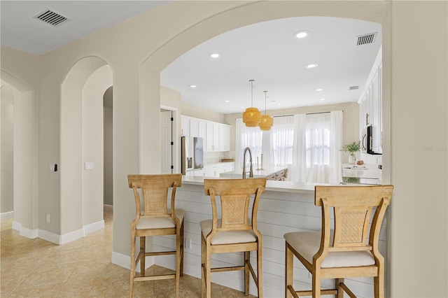 kitchen featuring hanging light fixtures, white cabinets, appliances with stainless steel finishes, a breakfast bar area, and tasteful backsplash