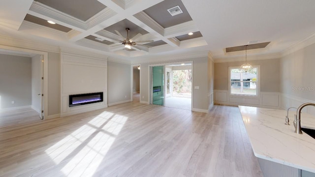 unfurnished living room featuring coffered ceiling, ceiling fan with notable chandelier, light wood-type flooring, beam ceiling, and crown molding