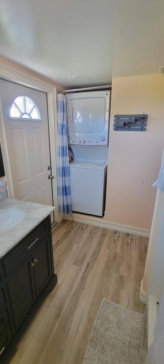 laundry room featuring stacked washing maching and dryer, sink, and light hardwood / wood-style flooring