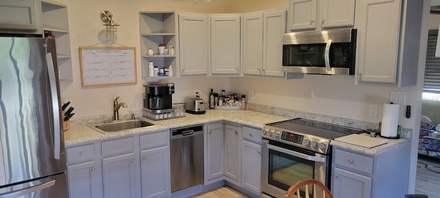 kitchen with light stone countertops, appliances with stainless steel finishes, light hardwood / wood-style flooring, and sink