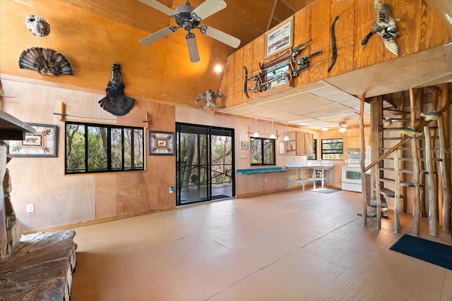 interior space featuring ceiling fan, high vaulted ceiling, and wood walls