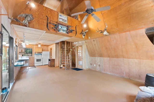 unfurnished living room with ceiling fan, wood walls, and vaulted ceiling