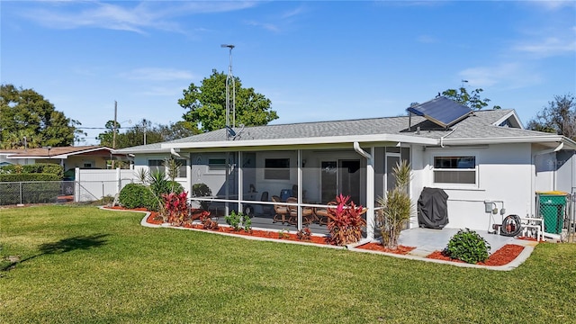 back of house featuring a lawn, a sunroom, and solar panels