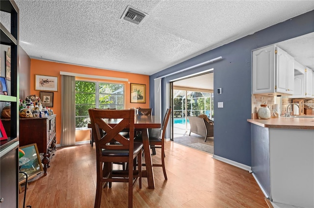 dining space with a textured ceiling, light wood-type flooring, a healthy amount of sunlight, and sink