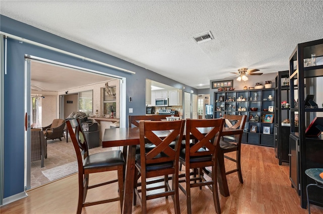 dining space with a textured ceiling, ceiling fan, and light hardwood / wood-style flooring