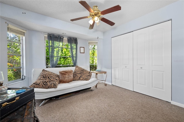 living area with ceiling fan, a textured ceiling, and carpet