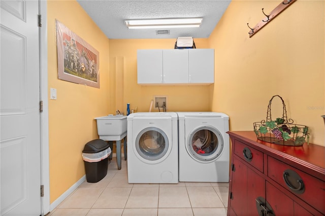 laundry room featuring cabinets, light tile patterned flooring, a textured ceiling, and washer and clothes dryer