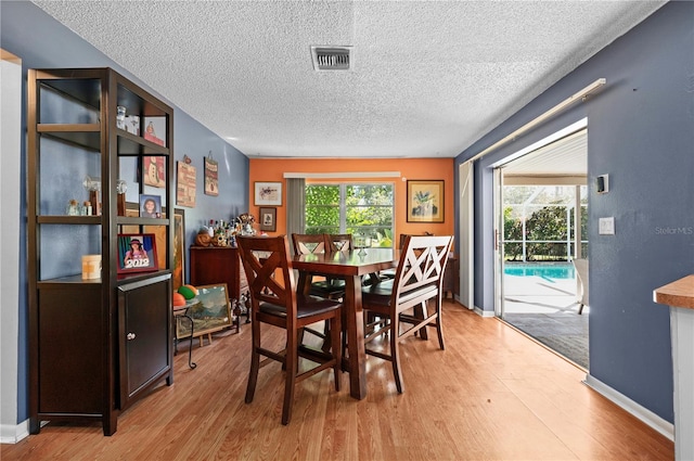 dining area with a textured ceiling and light hardwood / wood-style flooring