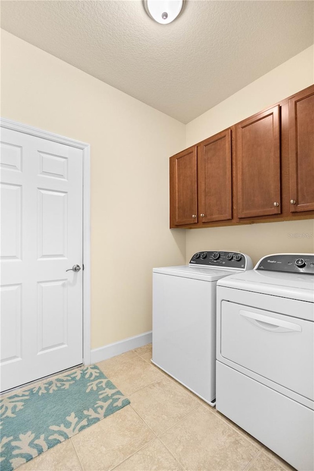 clothes washing area with light tile patterned floors, independent washer and dryer, a textured ceiling, and cabinets