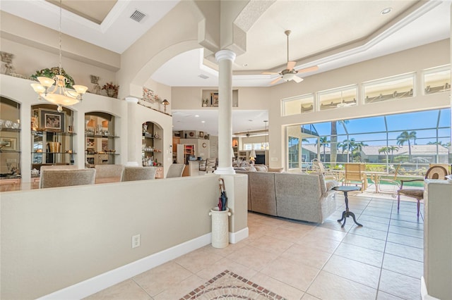 interior space with a raised ceiling, ceiling fan with notable chandelier, ornate columns, and light tile floors