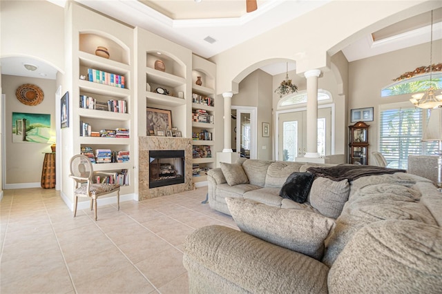 living room with a chandelier, light tile floors, a fireplace, built in shelves, and ornate columns