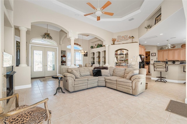 living room with a tray ceiling, ceiling fan, light tile floors, ornate columns, and french doors