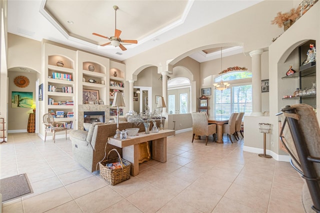 living room featuring light tile floors, ceiling fan with notable chandelier, ornate columns, and a raised ceiling