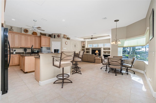 kitchen with light tile flooring, light brown cabinets, black refrigerator, and ceiling fan with notable chandelier