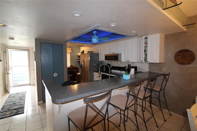 kitchen with a breakfast bar area, light tile patterned floors, kitchen peninsula, white cabinets, and stainless steel appliances