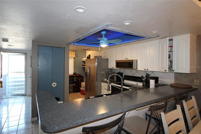 kitchen with appliances with stainless steel finishes, kitchen peninsula, ceiling fan, and light tile patterned floors